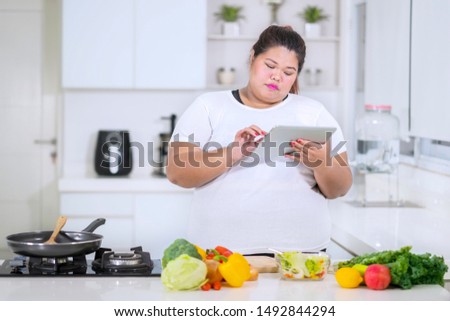 Picture of fat woman looking at recipes on a tablet while cooking in the kitchen