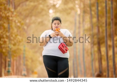 Picture of obese woman looks happy while using a mobile phone in the park with autumn season background