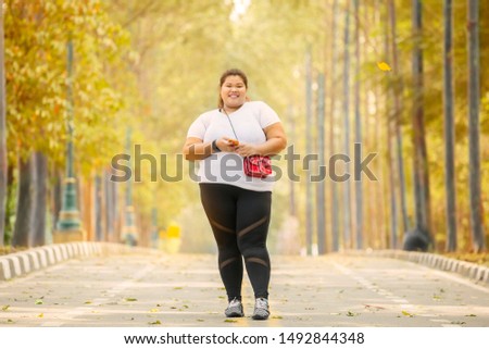 Picture of obese woman smiling at the camera while standing on the road at autumn time