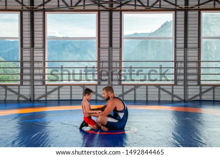 An adult male wrestler coach teaches the basics of wrestling and sets up a little boy to compete. The concept of child power and martial arts training. Teaching children Greco-Roman wrestling