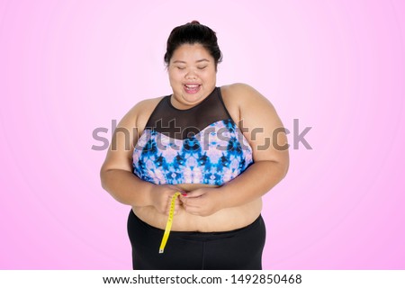 Picture of happy fat woman measuring her waistline after weight loss in the studio with purple color background