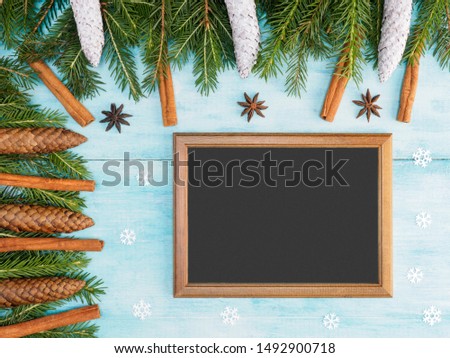 Blue wooden Christmas background with snow, fir branches, cones, cinnamon, anise, brown frame. Winter holidays concept