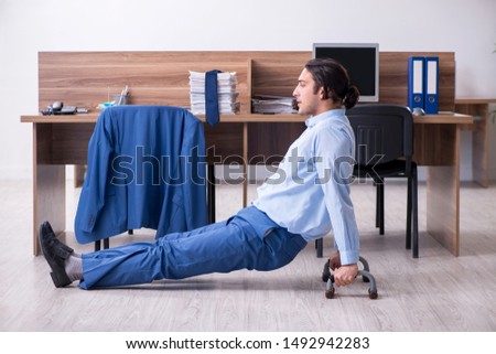 Young handsome businessman doing exercises at workplace 