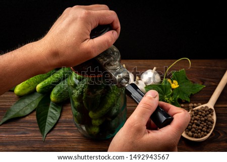 Machine for rolling metal caps on glass jar with fresh cucumbers on dark wooden  background.