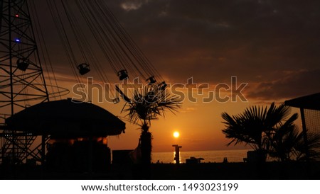 Swinging carousel roundabout chain ride at sunset. Entertainment on the beach, silhouettes of palm trees on a background of sea sunset