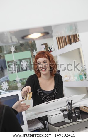 Young female owner taking payment in hairdressing salon