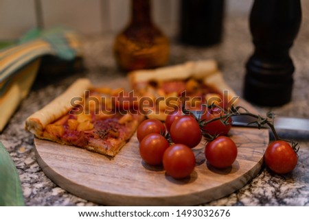 pizza on a cutting board with fresh tomato and oil in a bottle, with pepper in a black wooden pepper mill.