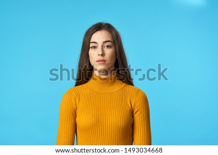 Charming young woman in a yellow sweater on a blue background cropped view                  