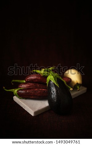 A variety of eggplants or aubergines shot on a piece of white marble against a dark burgundy background to give a painterly feel. 
