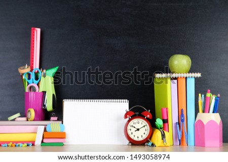 School supplies with blank sheet of paper on blackboard background