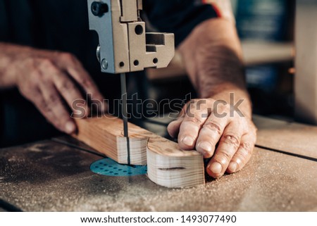 Carpenter working in workshop. Joiner labourer cuts wooden plank on jigsaw machine. Handwork, carpentry concept, woodworking.