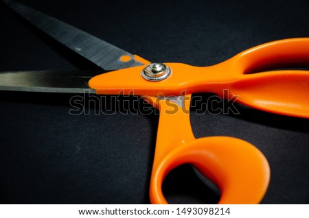 orange scissors on a black background in the hands