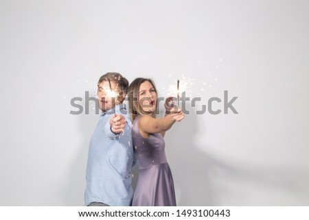 People, party and celebrations concept - young couple with sparklers staying back to back on white background