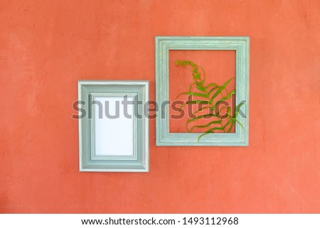 The green leaves are put in the picture frame, hung on the walls of orange cement, with patterns of colored lines and cracks of cement.