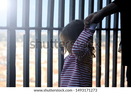 Adorable little girl holding her mother hand. Striped t-shirt worn by little girl. Iron bars in the background.