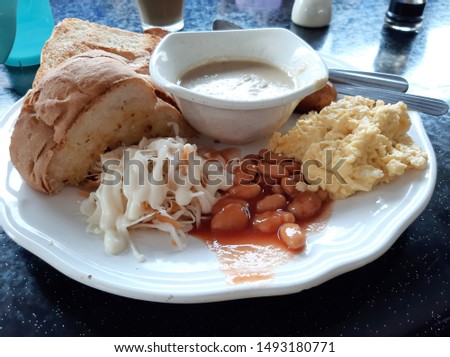 Flatlay picture of Malaysian style big western breakfast. The food consist of mushroom soup, bread, baked bean, jumbo sausage and coleslaw.