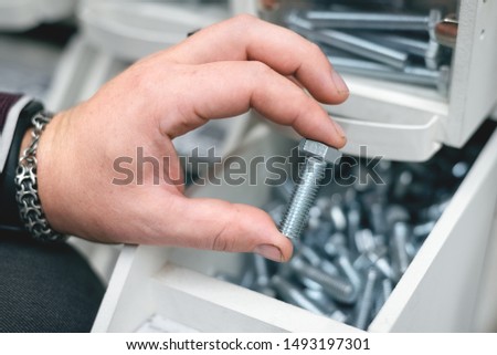 A buyer is choosing a bolt. A man is holding in hand one silver screw.
