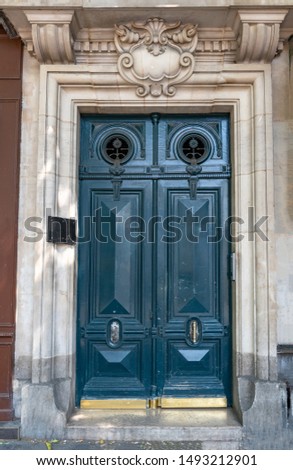 Sculptural ornate stone frame arch above aquatic blue painted antique door of old building in Paris France. Baroque architecture front door. Glossy paint wooden door surface with golden metal plates