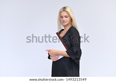 Portrait of a cute girl, a young blonde woman with beautiful curly hair in a black dress on a white background with a folder in her hands. Beauty, brightness, smile, emotions.