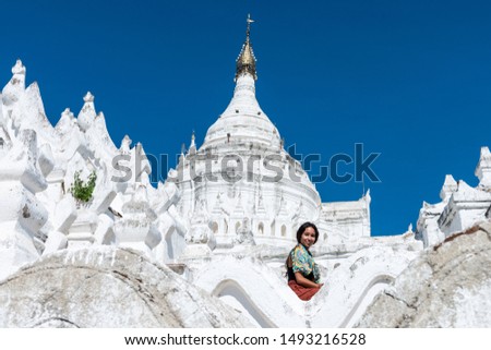 Horizontal picture of young tourist smiling at Hsinbyume Pagoda, a famous buddhist temple painted in white,  located close to Mandalay, Myanmar