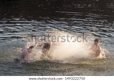 Adults splash each other in the water. Men play in the water. Silhouettes of teenagers playing in the pond.
