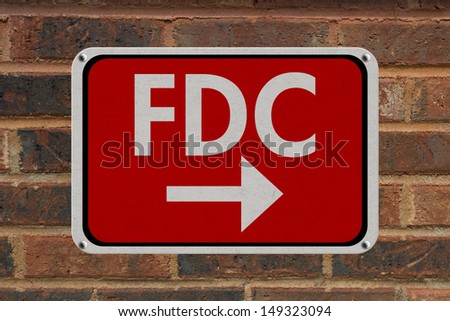 A red, white and black sign with word FDC on a brick wall, FDC this way