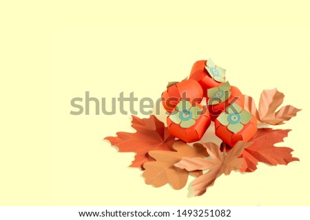 Paper persimmon and autumn leaves on yellow background. Paper art and craft. Trendy hobby. Autumn food art concept. Copy space