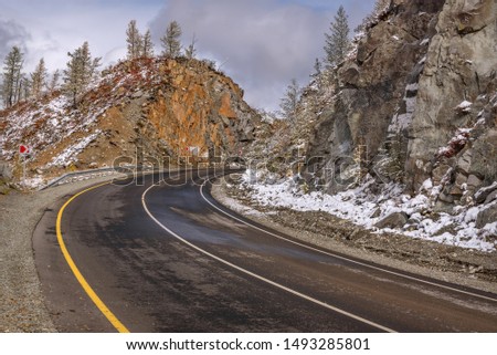 Scenic view of the hairpin bend wet winding road through the pass, part of the mountain serpentine, in autumn cloudy weather with first snow