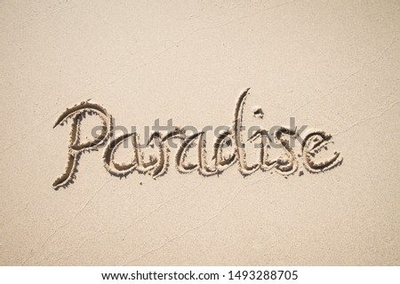 Paradise message handwritten on the smooth sand of an empty beach with copy space