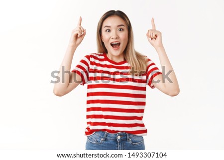 Excited impressed cheerful young asian blond girl happy finally product in stock pointing up index finger amused telling you cool copy space open mouth smiling fascinated standing white background