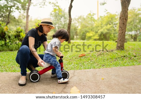 Young asian mother teaching her adorable toddler girl to ride the bike for the first time while spending time outing together in the morning, concept mother and child love, family time and activity.