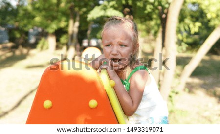 Portrait of little beautiful girl playing on the playground near trees and screaming