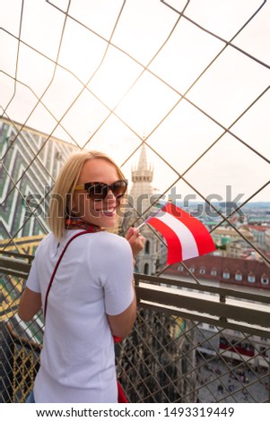 A woman enjoys the panorama of Vienna and the sunset from the viewpoint of St. Stephen's Cathedral on Stefanplatz and holds the flag of Austria in her hands. Travel to Austria