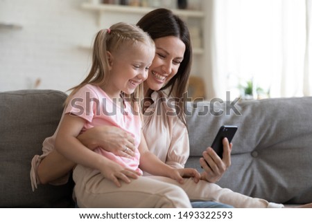 Cheerful little daughter sitting on mother lap family spend free time in internet using smart phone, modern tech wifi usage, bad habit kid and electronic gadget, parental control online safety concept
