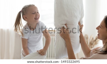 Cheerful mother lovely daughter holding white pillows fighting on bed close up image, laughing preschool girl kid playing enjoy weekend with older sister, have fun, leisure active, free time concept