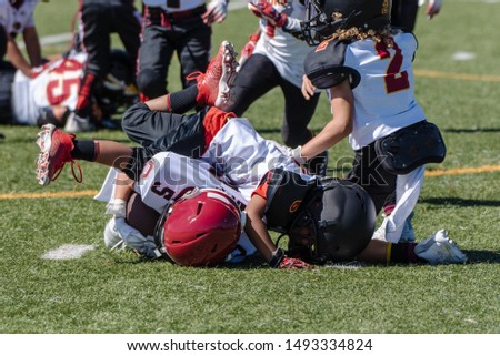 Offensive youth football player is tackled and at bottom of pile during game at stadium. Royalty-Free Stock Photo #1493334824
