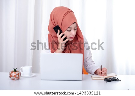 Muslim woman work with computer, hijab muslim girl at office and she is talking on mobile phone, support, contact or customer service concept photo