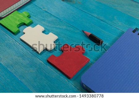 Problem solving and teamwork concept with colorful puzzle pieces in red, white and green on a blue table with notebooks and a pencil stub in a high angle view