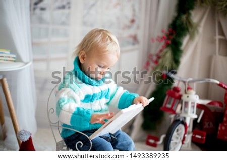 Cute little toddler child with colorful book at home on a snowy winter day, christmas decoration