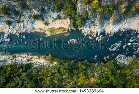 Aerial top-down photo of a blue river in a mountain canyon with green forest and a touristic camp
