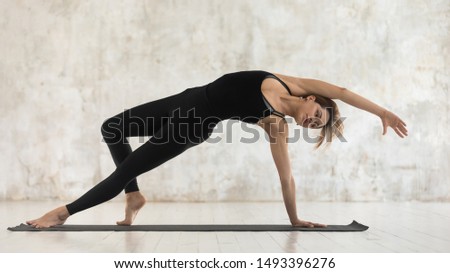 Beautiful woman wearing black sportswear practicing yoga, standing in Wild Thing pose, attractive sporty girl doing Camatkarasana exercise, working out at home or in yoga studio, horizontal banner