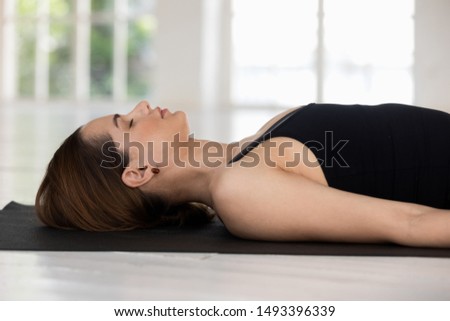 Young woman with closed eyes practicing yoga, doing Savasana exercise, meditating, relaxing in Corpse pose, sporty girl wearing black sportswear working out at home or in yoga studio close up Royalty-Free Stock Photo #1493396339