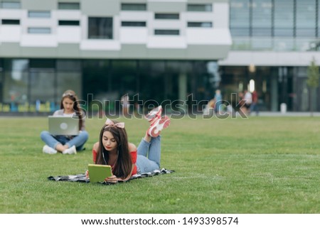 Work on freelance. Relax and be happy. Student learning. Two pretty girls friends sitting on the green grass.
