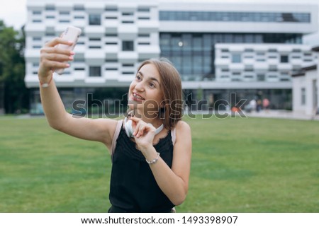 Teenage girl taking a selfie on smart phone outdoors in summer. Young woman photographing herself smiling. Mild retouch, vibrant, natural light, horizontal.