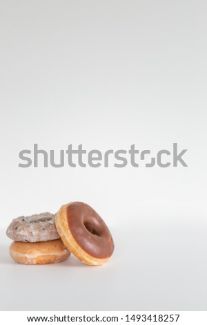 Three donuts stacked on one another, chocolate iced, blueberry cake, and plain glaze, white background, copy space