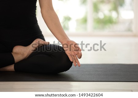 Woman practicing yoga, relaxing in Lotus pose on mat, Padmasana exercise close up, mudra hand and feet close up, girl wearing black sportswear working out, meditating in yoga studio or at home Royalty-Free Stock Photo #1493422604