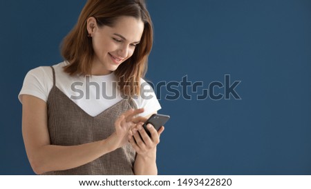 Smiling beautiful woman using mobile phone apps isolated on blue studio background, attractive young female chatting online, typing, looking at cellphone screen, reading good news, horizontal banner