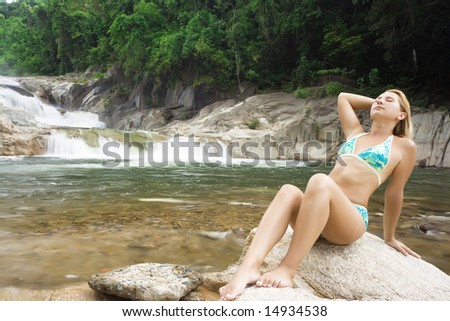 Young woman relaxing on the stone over waterfall background