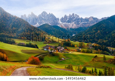 Picturesque autumn scenery in Santa Maddalena village with church, roads and meadows on foreground and Odle mountain peaks on background. Dolomite Alps, South Tyrol, Italy.