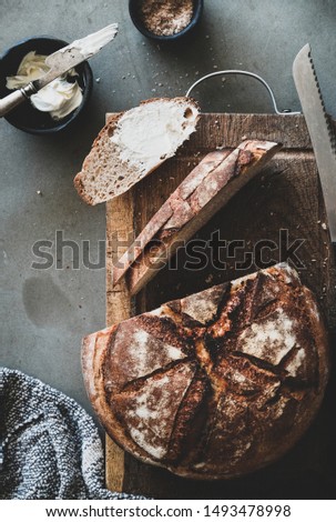 Bread and butter breakfast or snack. Flat-lay of freshly baked sourdough bread loaf and slices with butter and smoked salt over grey concrete table background, top view